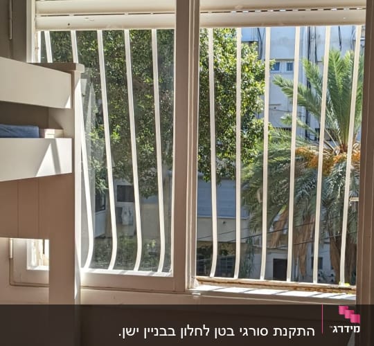 חלון עם סורגים לבנים ותריסים פתוחים
